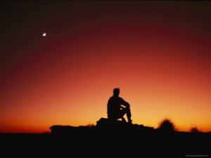 silhouette-of-sitting-man-looking-at-the-sunset-and-the-moon